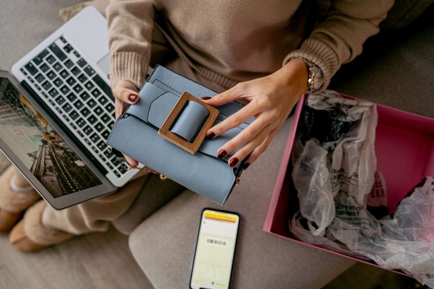 Mulher usa um laptop enquanto desembrulha uma bolsa comprada pela internet em casa.