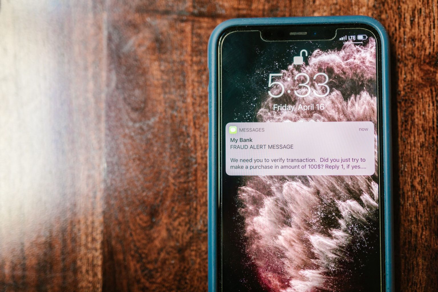 Celular exibindo uma notificação de alerta sobre fraude sobre uma superfície de madeira.